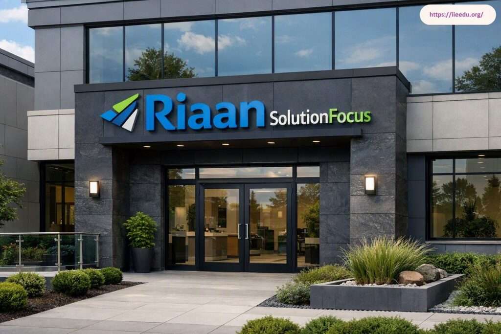 Modern office building exterior for Riaan Solution Focus featuring dark stone cladding, glass double entrance doors, prominent blue and green corporate header signage, external wall lighting, and manicured landscaping.
